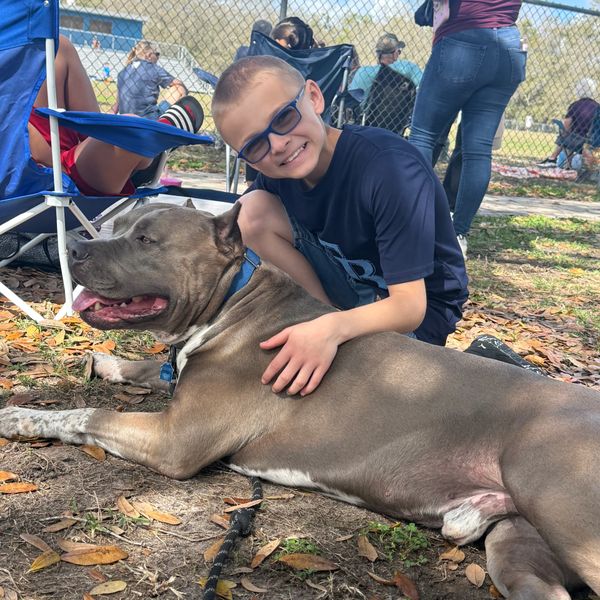 A boy smiles while hugging his large dog outdoors at a park event.