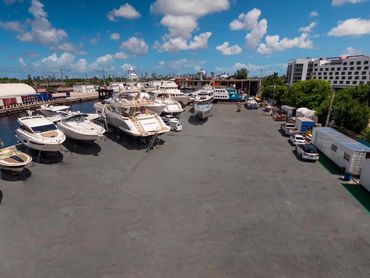 Yachts and boats docked on a sunny day at a marina with city skyline in background.