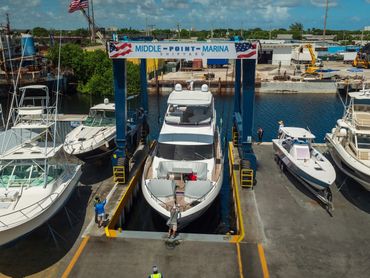A large yacht being lifted at Middle Point Marina shipyard with workers guiding it.