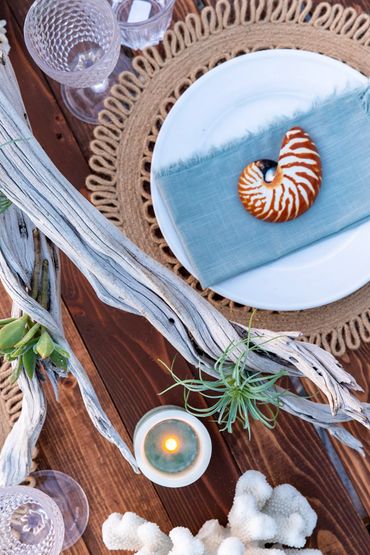 closeup of table setting featuring, driftwood, airplants, candles, charger, plate, napkin, seashell