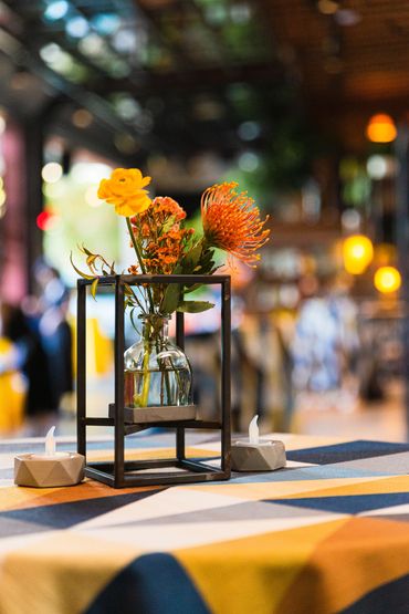 metal frame vase centerpiece with yellow + orange flowers on orange, blue + yellow color block linen