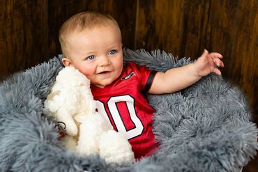 baby boy in his basket filled with blanket wearing a football jersey and big smiles
