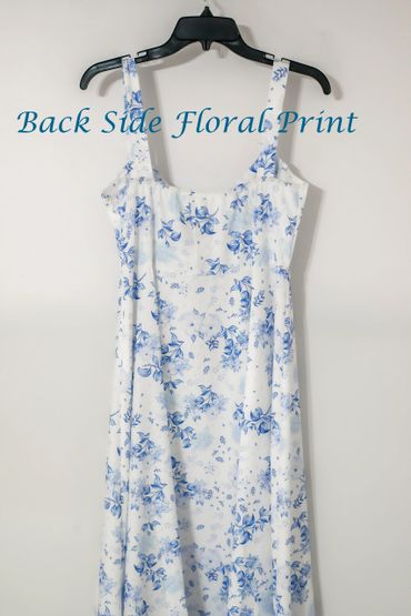 White dress with blue floral print hanging on a black hanger.
