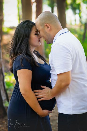 Pregnant couple sharing a tender moment in a forest setting.