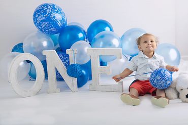 One year baby boy sitting with his blue balloons and the letters that spells ONE