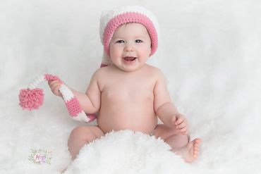 6 month old baby girl posing for her Milestone photo session wearing a cute pink and white cap
