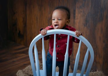 6 month old baby boy standing on his wooden chair backwards with a big smile on his face