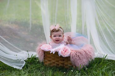 9 month old baby girl sitting in a brown basket outside