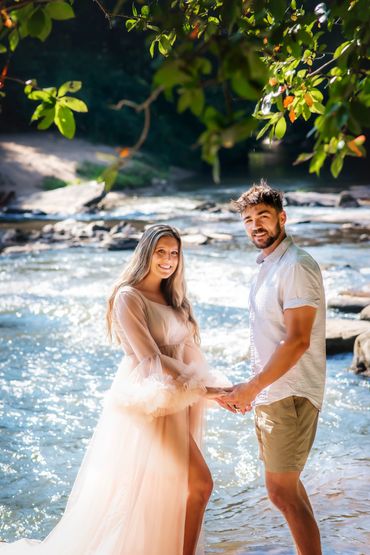 Young couple standing face to face taking Maternity photos at Hurricane Shoal park with water