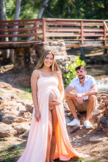 Young woman taking Maternity photos as her husband looks on at Hurricane Shoals park