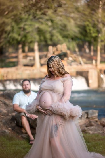 beautiful woman posing for her maternity photo at Hurricane Shoals park by the water as her husband