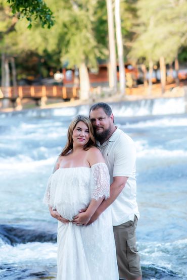 couple posing for their Maternity photos in a beautiful white dress at Hurricane Shoals Park
