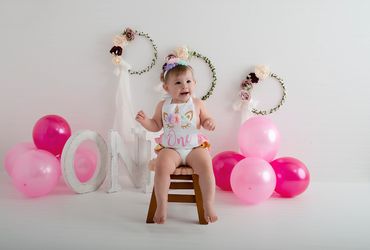 One year old sitting on a stool with balloons all around for a cakesmash birthday