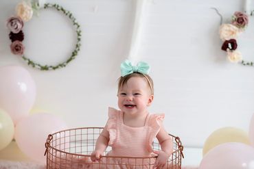 One year old sitting in a wire basket for her cake smash session