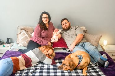 In home newborn session with mom and dad and big sister laying on their bed with the family dog