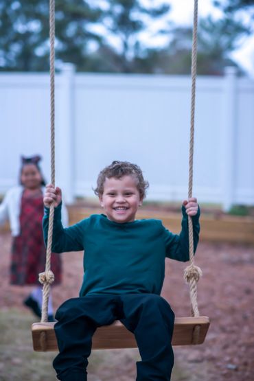 3 year old playing on a tree swing with his big sister standing behind him