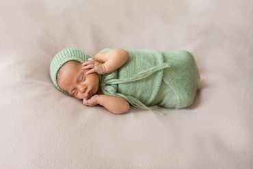 In home newborn session with baby laying on a gentle bed green knitted wrap and bonnet.