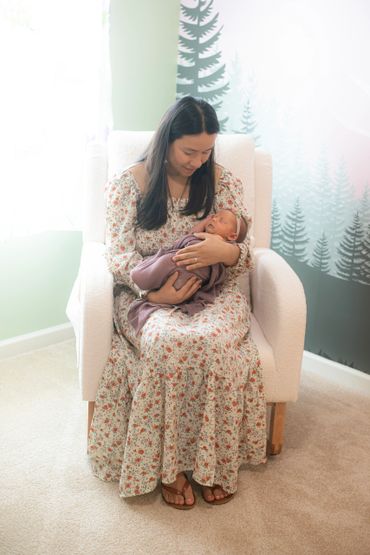 Mother in floral dress holding sleeping newborn in cozy nursery.