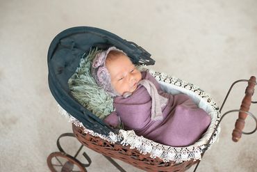 In Home Newborn session with baby wrapped in lavendar and matching bonnet laying in antique stroller