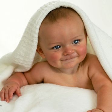 6 month old baby boy laying on his tummy on the beanbag with a blanket over his head and big smiles