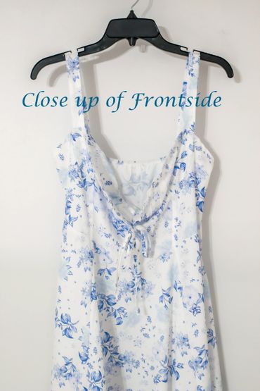 White dress with blue floral print hanging on a black hanger.
