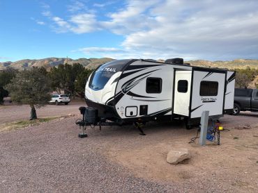 White and black travel trailer parked outdoors on a gravel lot.