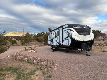 A modern RV parked in a scenic campsite under a cloudy sky.