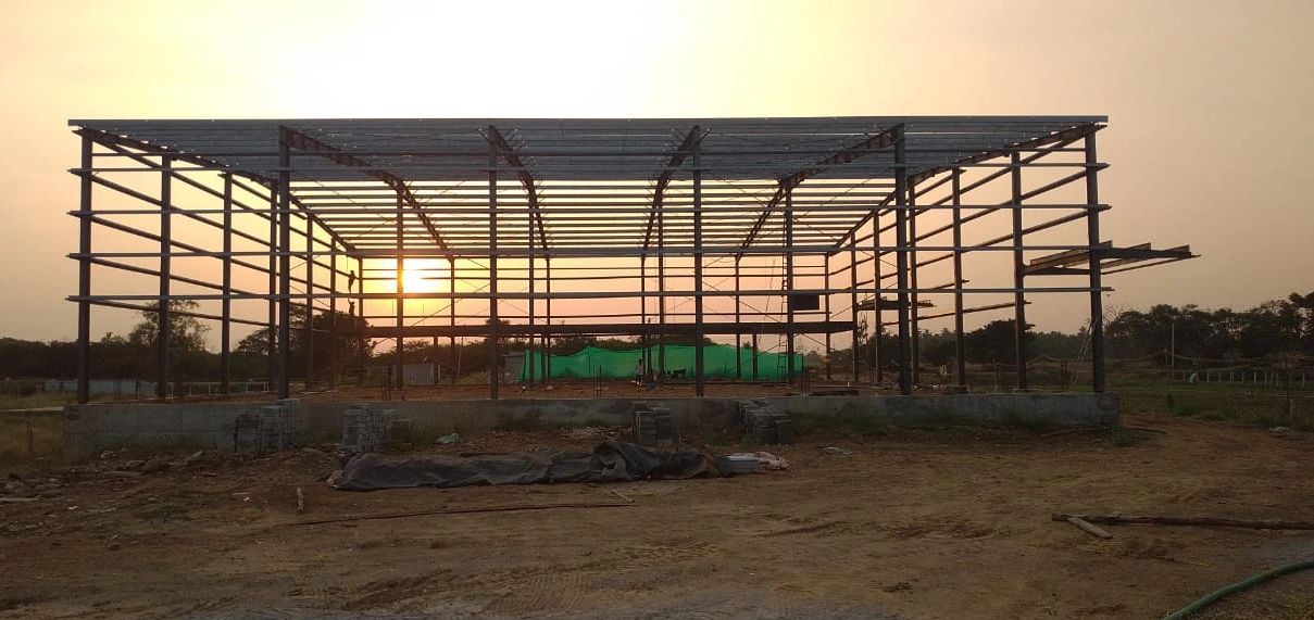 Steel frame structure under construction at sunset in an open field.