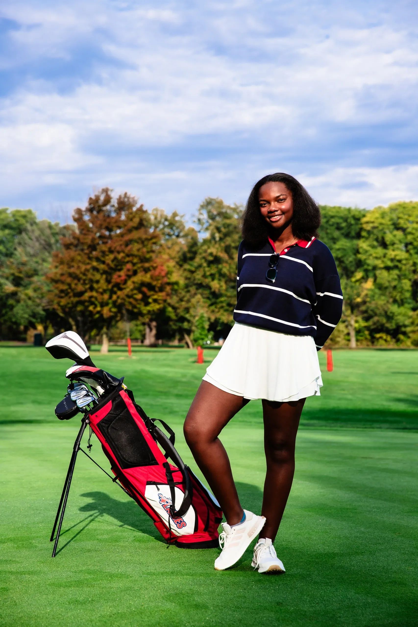 Smiling young woman posing with golf bag on lush green course.