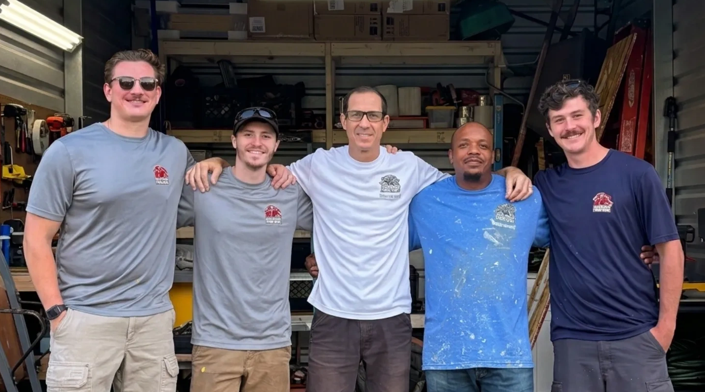 Five men standing together in a workshop, smiling.