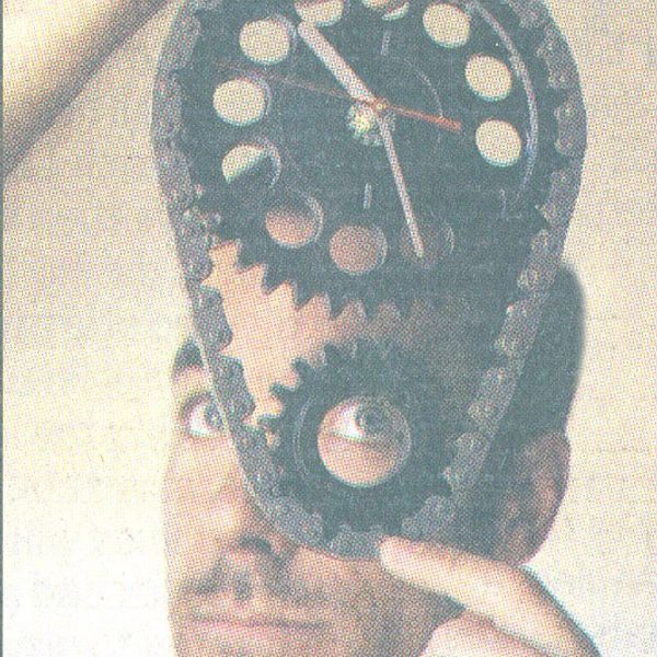 Artist, Steven Shaver peeking through the gear of a car parts clock that he created.