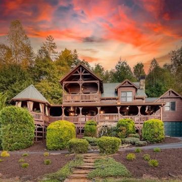 A rustic wooden house surrounded by greenery during a vibrant sunset.