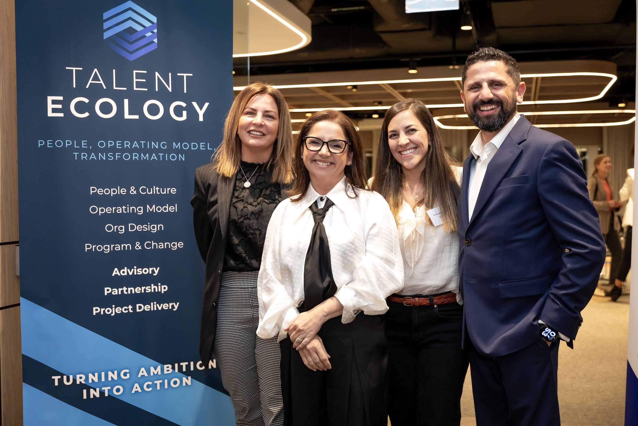 Four smiling professionals standing beside a Talent Ecology banner.