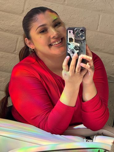 Smiling woman in a red shirt taking a colorful mirror selfie.