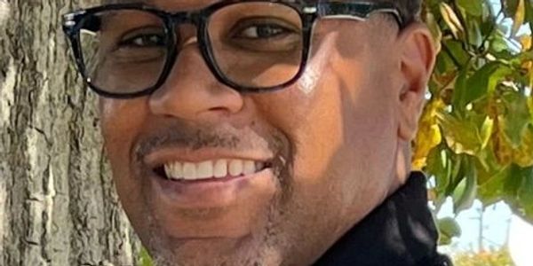 Smiling man wearing glasses outdoors near a tree.