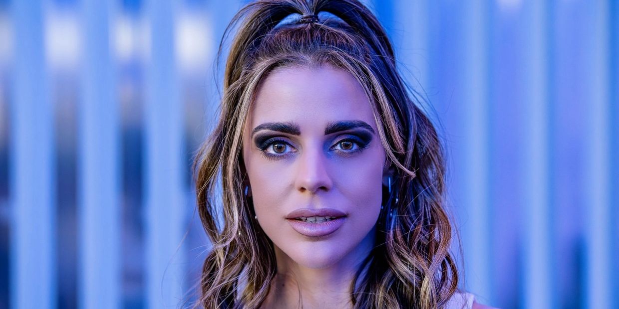 Close-up portrait of a woman with wavy hair and intense eyes under blue lighting.