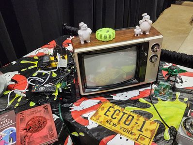 Ghostbusters-themed table with vintage TV, toys, and memorabilia.