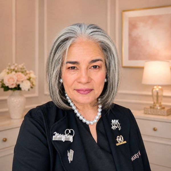 Confident woman with grey hair wearing a black jacket and pearl necklace.