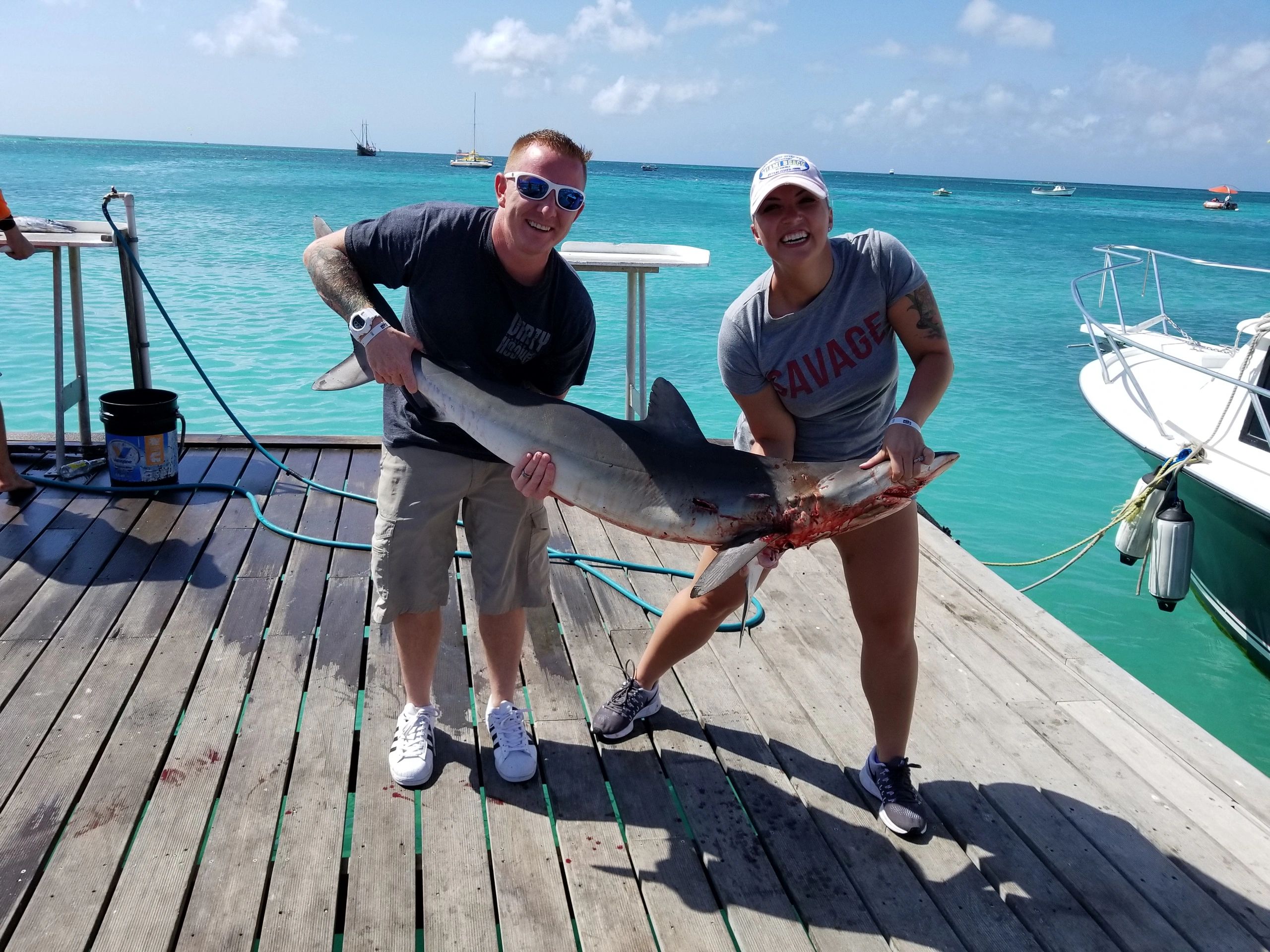 man and woman standing on a dock and holding a dead shark in Aruba