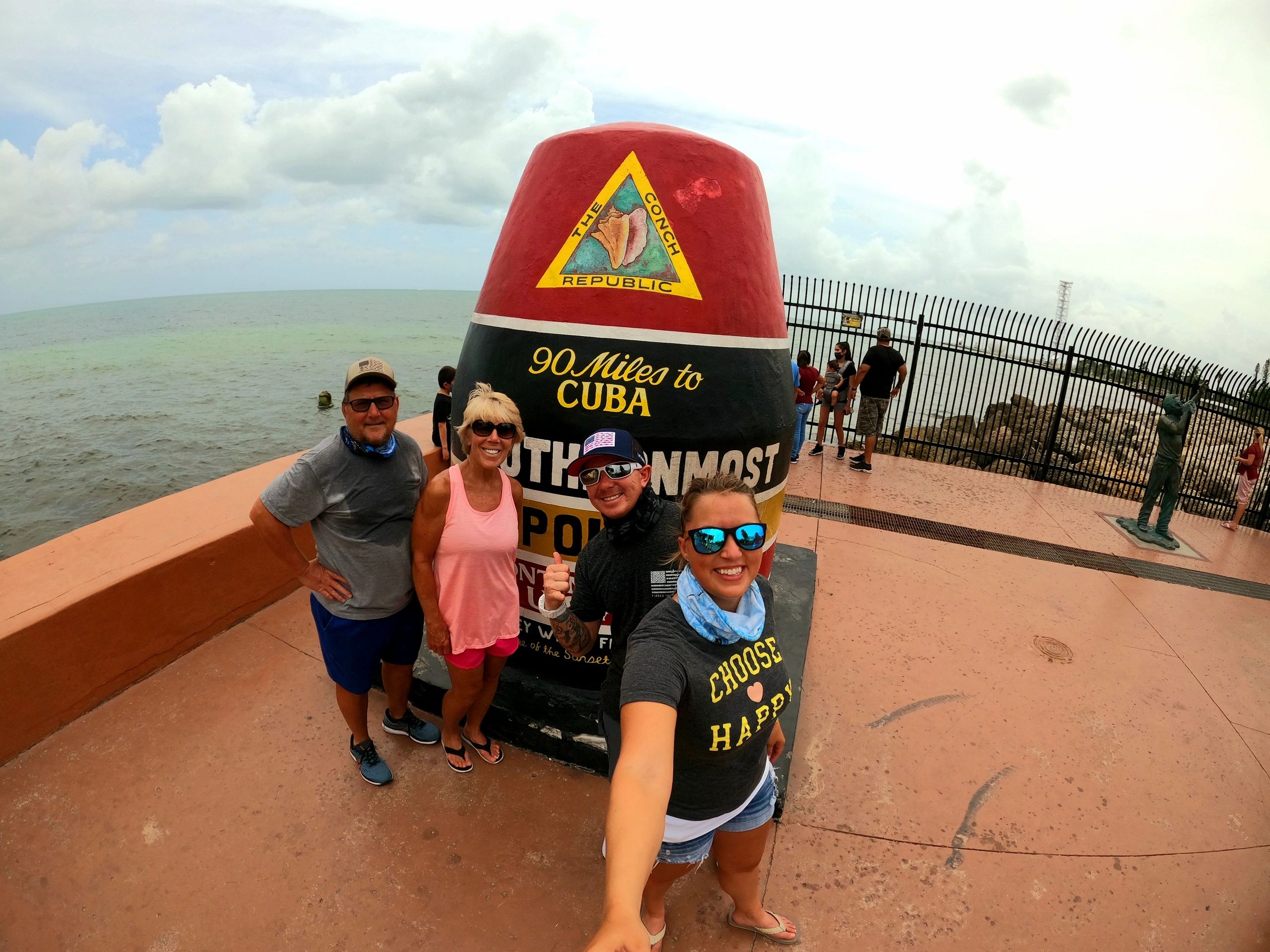 four people standing in front of statue of the southern most point in key west florida 