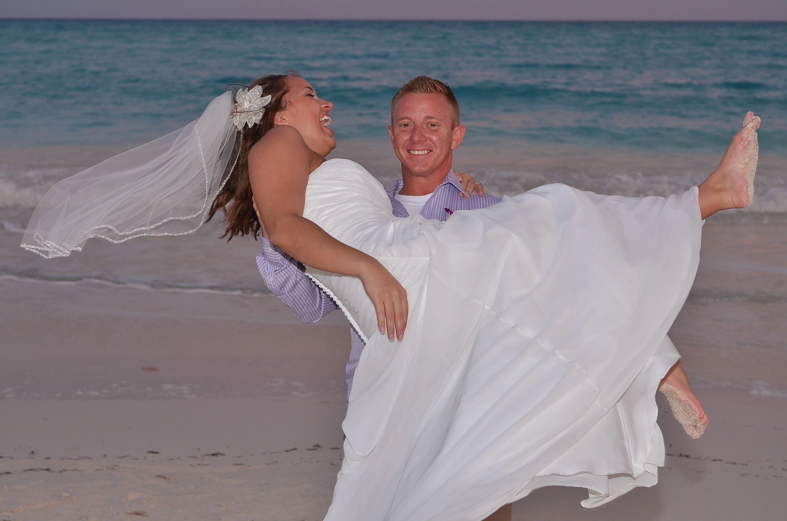 Man holding woman in a wedding dress on a beach