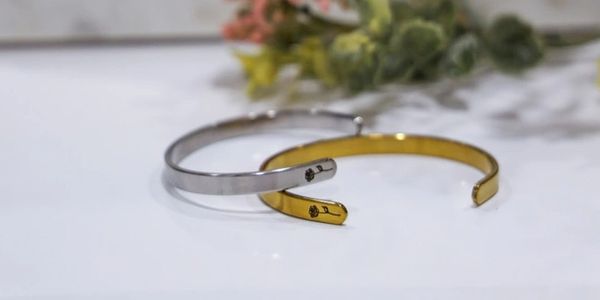Minimalistic silver and gold bangles on a white surface with soft floral background.