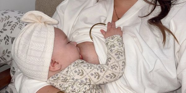 Mother breastfeeding her baby while sitting on a couch, dressed in white and floral patterns.