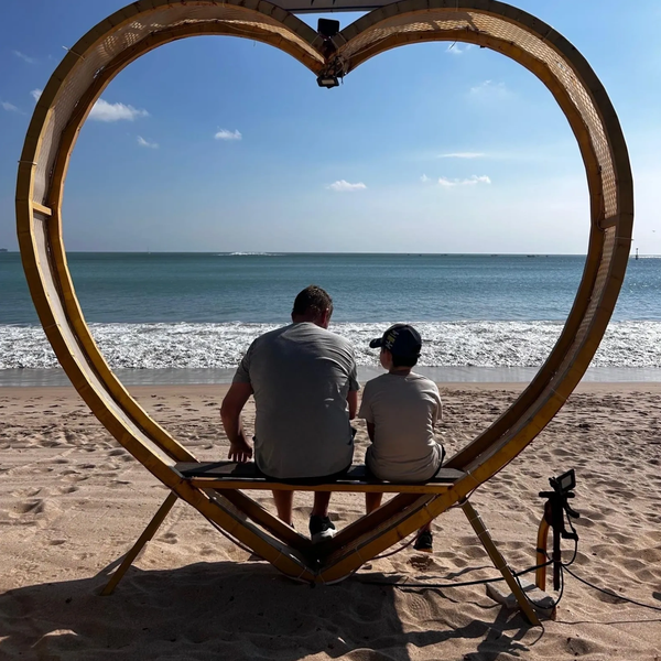Father and son sitting on a heart-shaped bench by the beach, enjoying the ocean view.