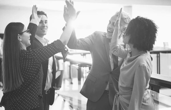 Four colleagues enthusiastically high-fiving in a bright office.