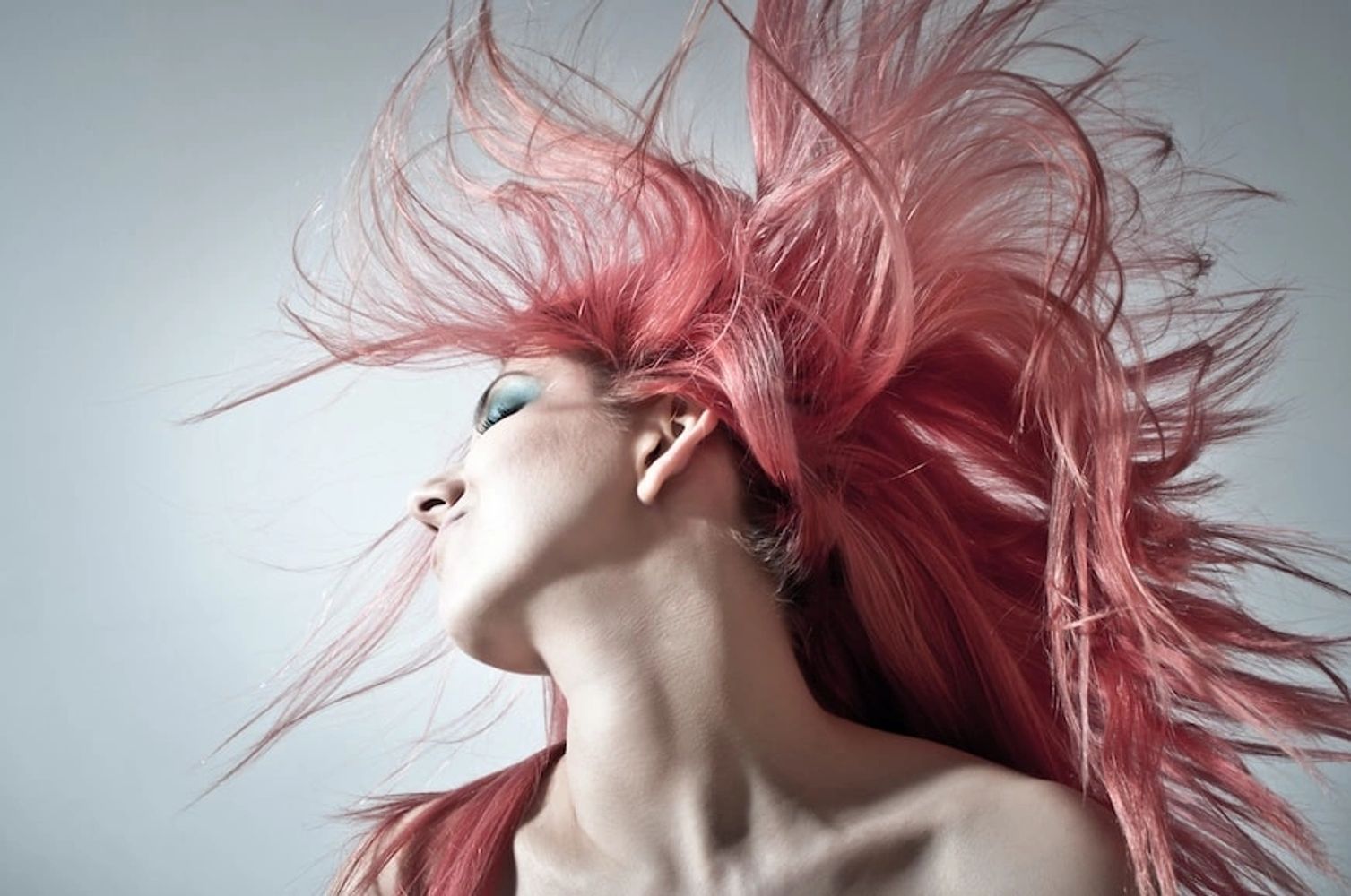Woman with vibrant pink hair flowing dynamically against a plain background.