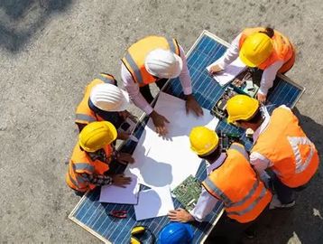 Construction workers in safety gear discussing plans around solar panels.