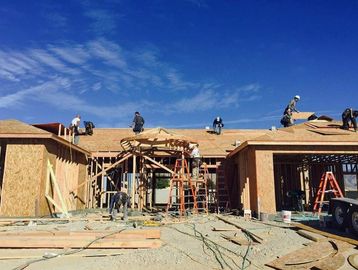 Workers building a wooden house frame under a clear blue sky.