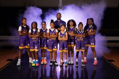 Girls' basketball team posing with coach amid stage smoke.