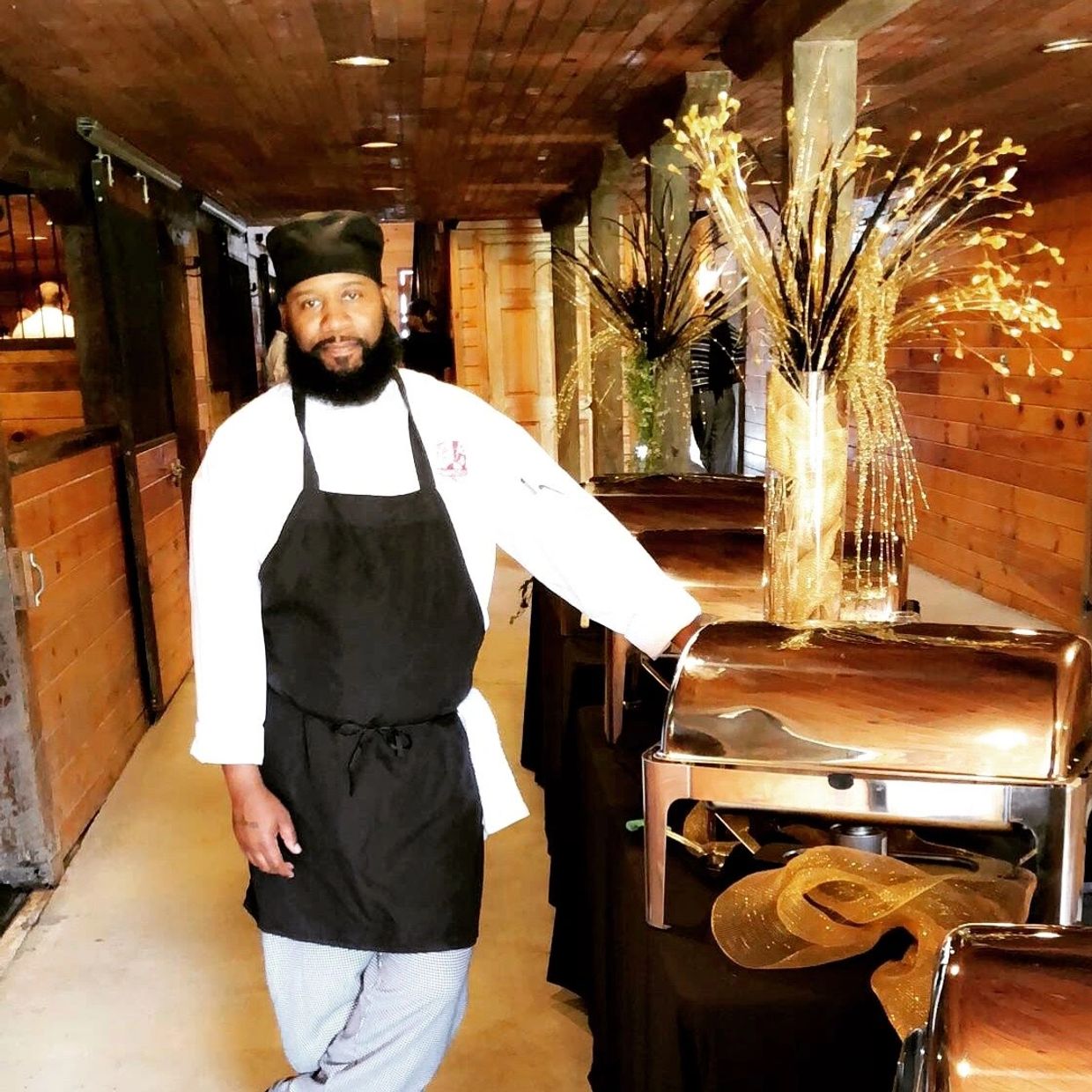 Chef in black apron standing by a buffet setup with golden decor.